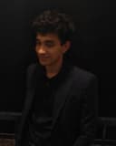 Vatsalya Betala in a dark blazer, smiling and looking off to the side, against a night-time background.