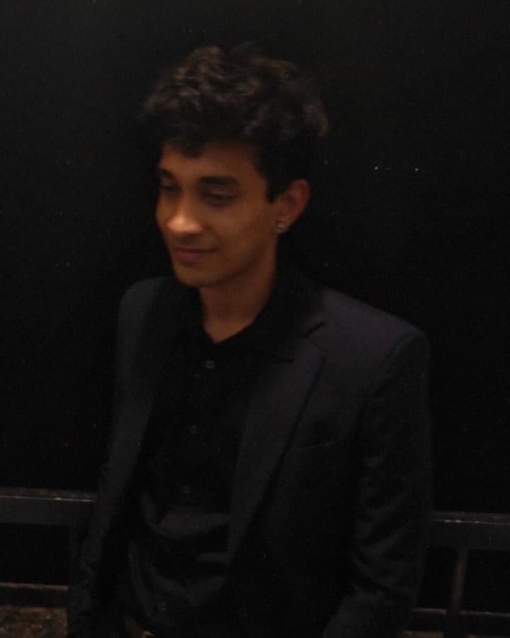 Vatsalya Betala in a dark blazer, smiling and looking off to the side, against a night-time background.